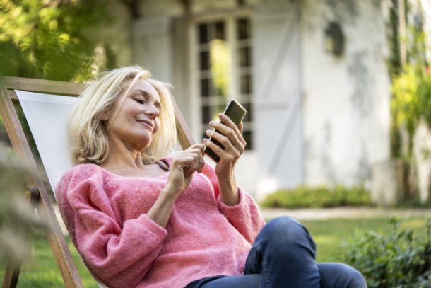 Vrouw zit in tuinstoel met haar smartphone te spelen