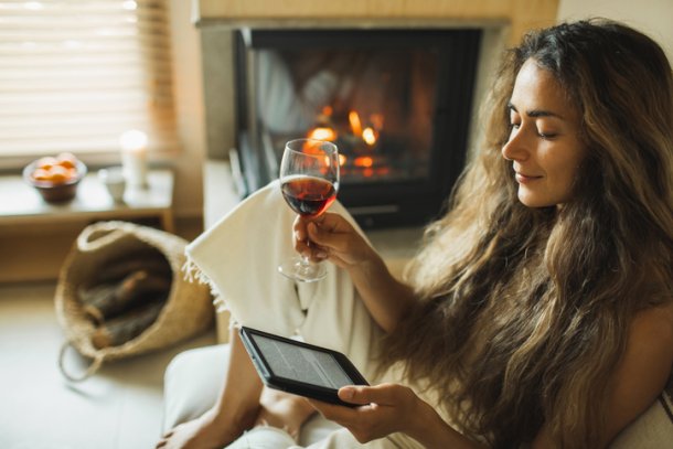 Knappe vrouw met lang haar leest uit e-reader met glas wijn in haar hand