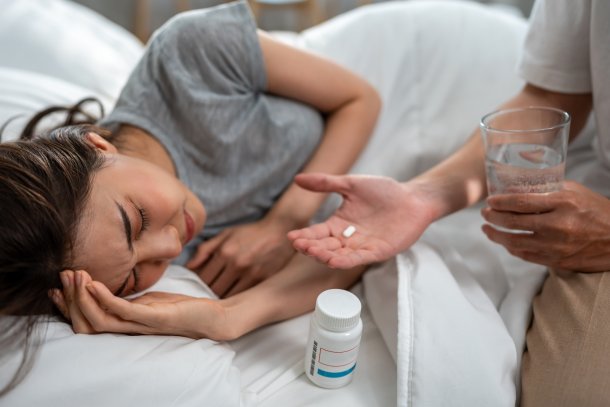 Vrouw ligt ziek op bed en krijgt paracetamol