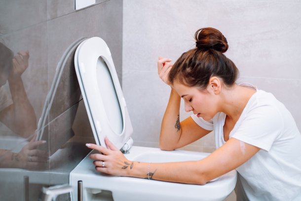 Jonge vrouw hangt over rand van het toilet