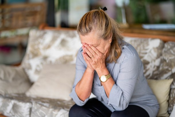 Oudere dame op de bank met handen in het gezicht