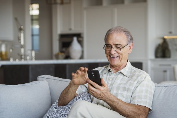 Man is vrolijk met telefoon bezig in huiskamer