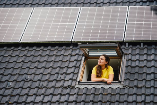 Dak met zonnepanelen, knappe vrouw kijkt uit het raam
