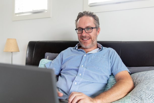 Man zit op de bank blij te spelen met zijn laptop