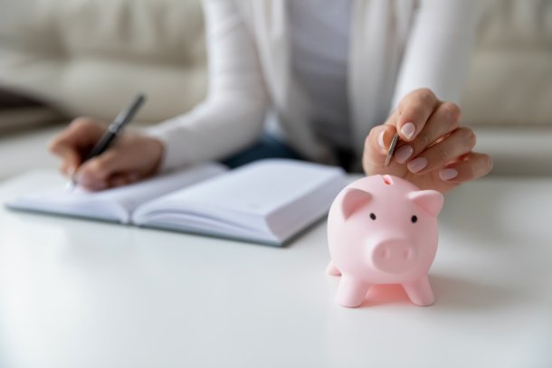 Vrouw schrijft haar uitgaven op en stopt geld in spaarvarken