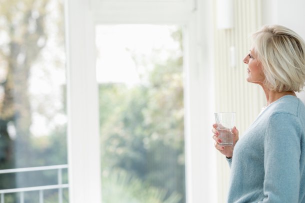 Vrouw drinkt glas water en kijkt naar buiten door het raam