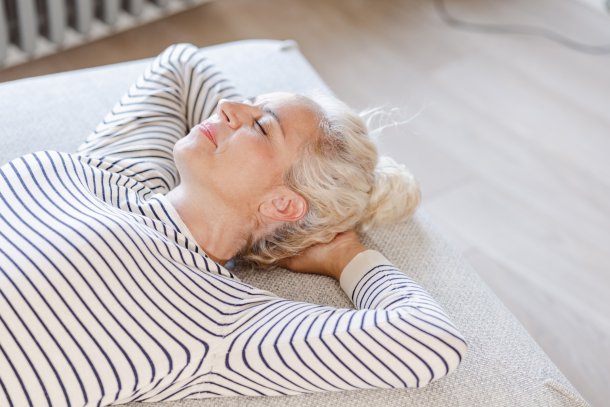 Vrouw ligt op haar rug zonder kussen op haar bed 