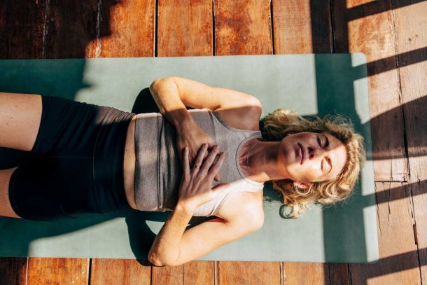 vrouw doet ademhalingsoefeningen op yogamat