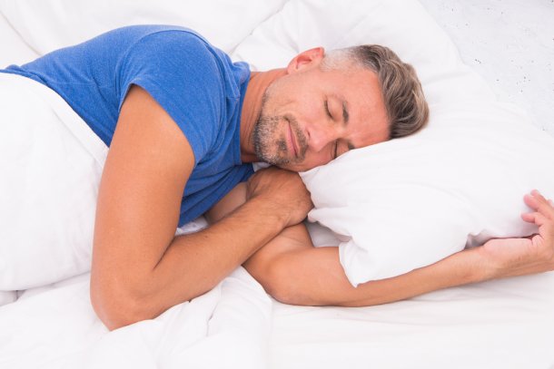Man ligt op zijn linkerzij te slapen in een bed met wit beddengoed