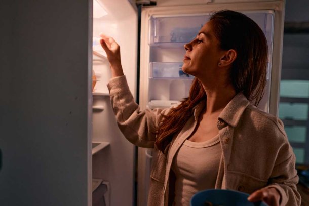 Vrouw staat in de nacht bij de koelkast