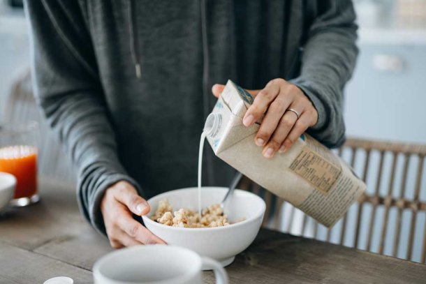 Vrouw schenkt sojamelk over cornflakes