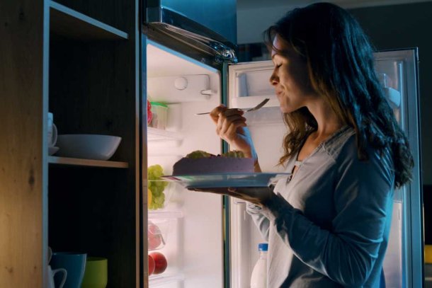 Vrouw eet 's nachts voor de koelkast