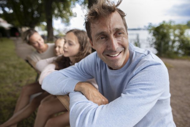 Man kijkt weg van camera met familie op achtergrond, weiland met houten palen