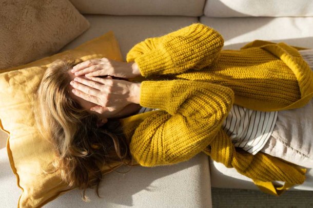 Vrouw met handen voor haar ogen ligt op de bank