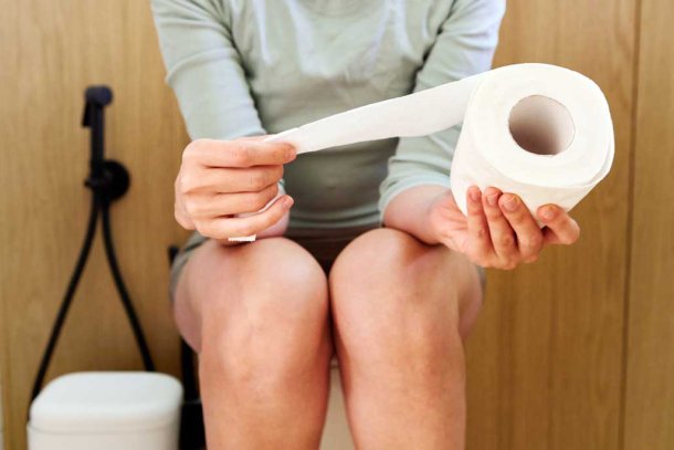 Vrouw met een wc-rol in haar hand zittend op het toilet