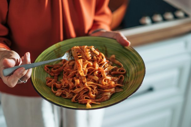 Vrouw in de keuken met bord pasta in haar handen