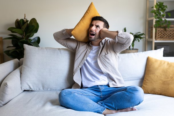 Man met kussen en hand tegen zijn oren, heeft last van herrie van de buren