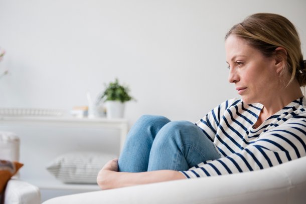 Vrouw zit op de bank thuis staart zorgelijk voor zich uit