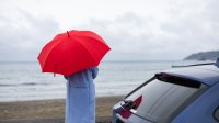 Regen vrouw met paraplu met auto aan het strand